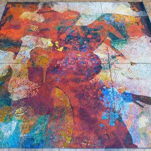 Abstract colorful artwork with dominant red, orange, and blue hues on a tiled surface.