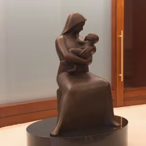 Bronze statue of a seated woman wearing a hood, cradling a baby in her arms.