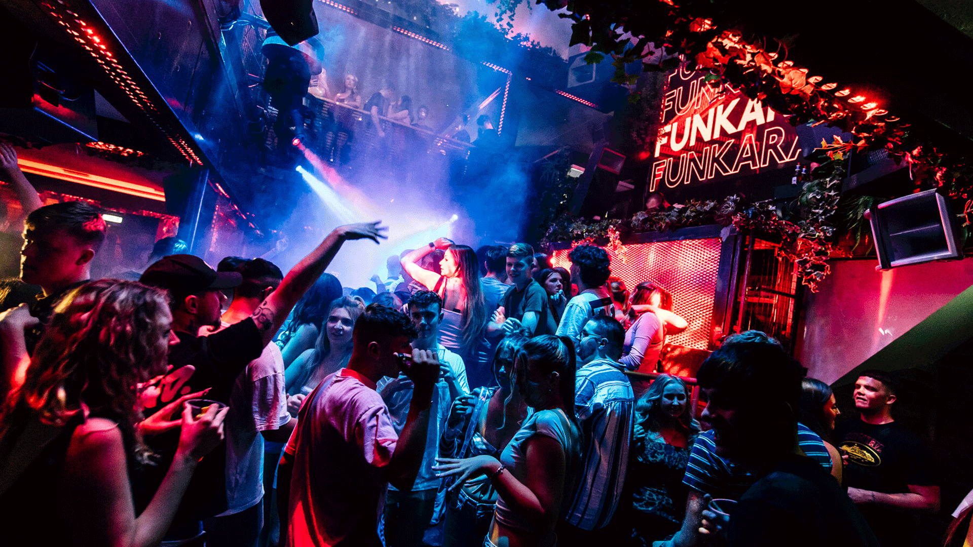 A vibrant nightclub scene at Thompsons Garage in Belfast, with people dancing in a lively atmosphere. Colorful lights and smoke fill the space, highlighting the energy of the DJ event playing house music during a club night. Belfast nightlife is prominently featured.