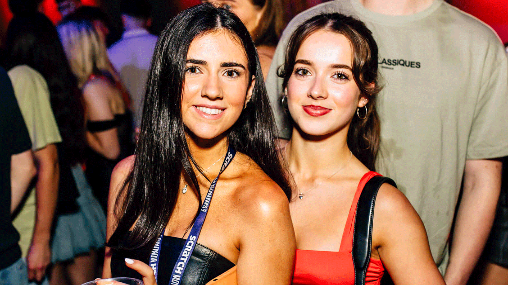 Two young women smiling and posing for a photo at an event in a nightclub. Bright lights and a crowded atmosphere suggest a lively club night, possibly featuring house music at Thompsons Garage in Belfast.