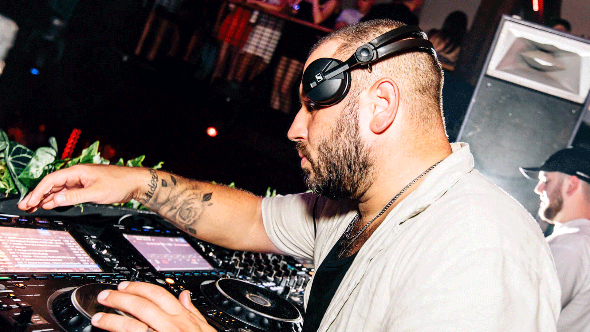 A DJ performing at a vibrant nightclub, manipulating turntables and equipment with colorful lights in the background. The setting reflects the lively atmosphere of Belfast nightlife, showcasing a club night focused on house music and DJ events.