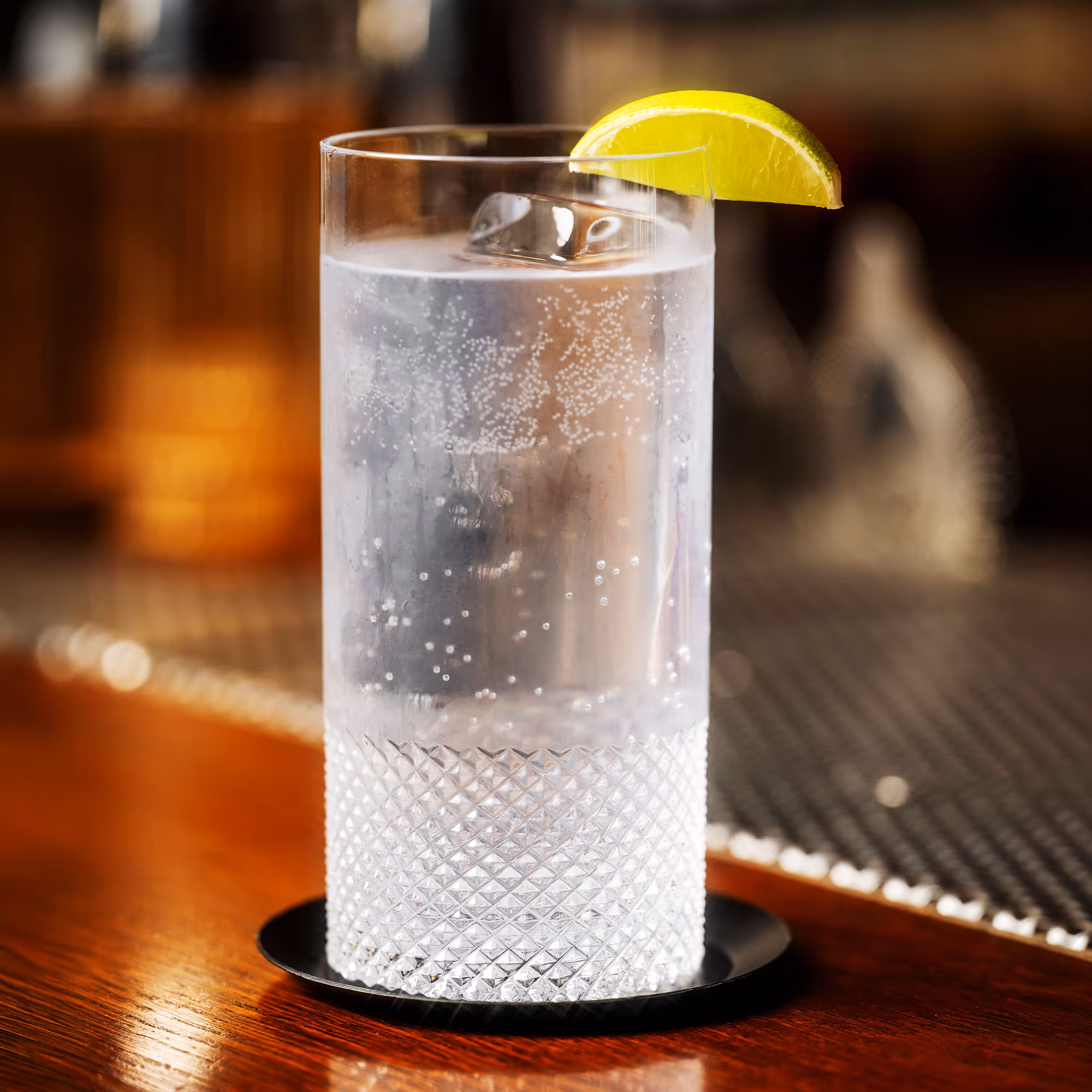 Tall textured glass filled with sparkling water and ice, garnished with a lime wedge on the rim, on a wooden surface.
