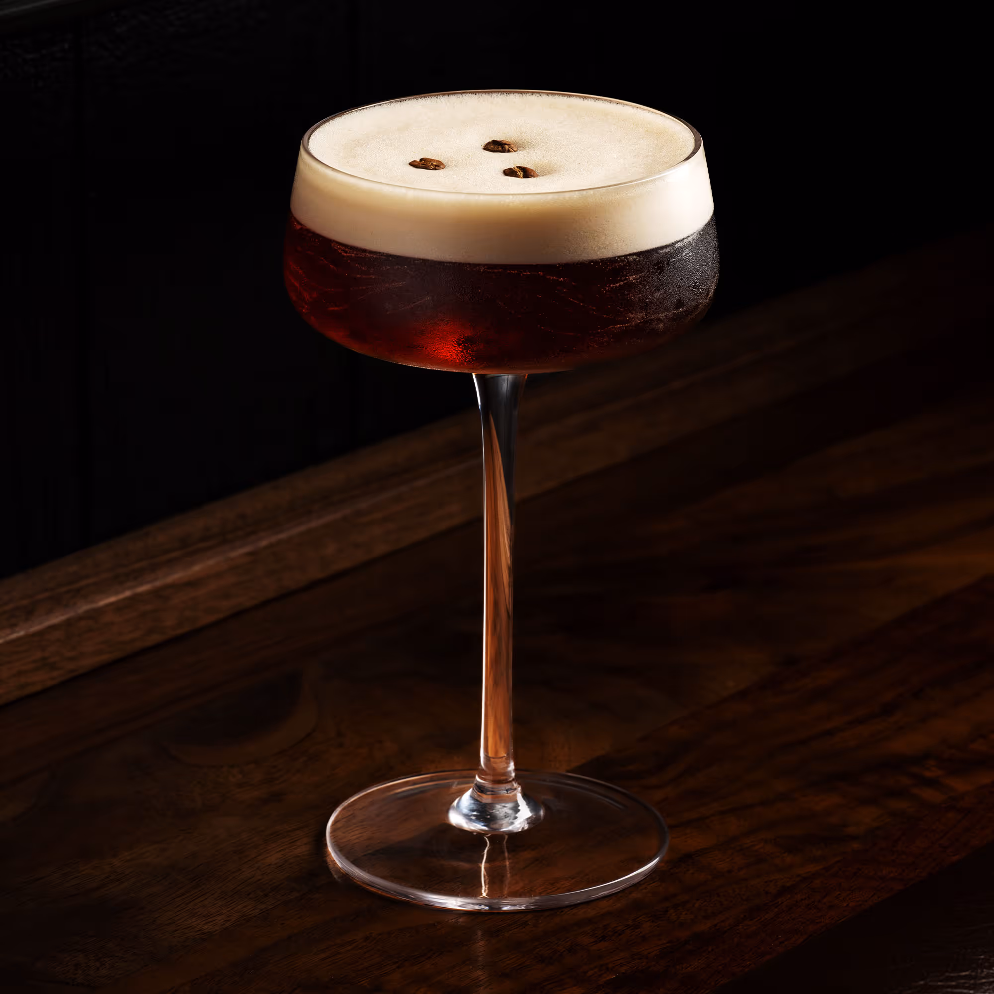 Espresso martini cocktail in a coupe glass with creamy foam topped with three coffee beans on a wooden surface.
