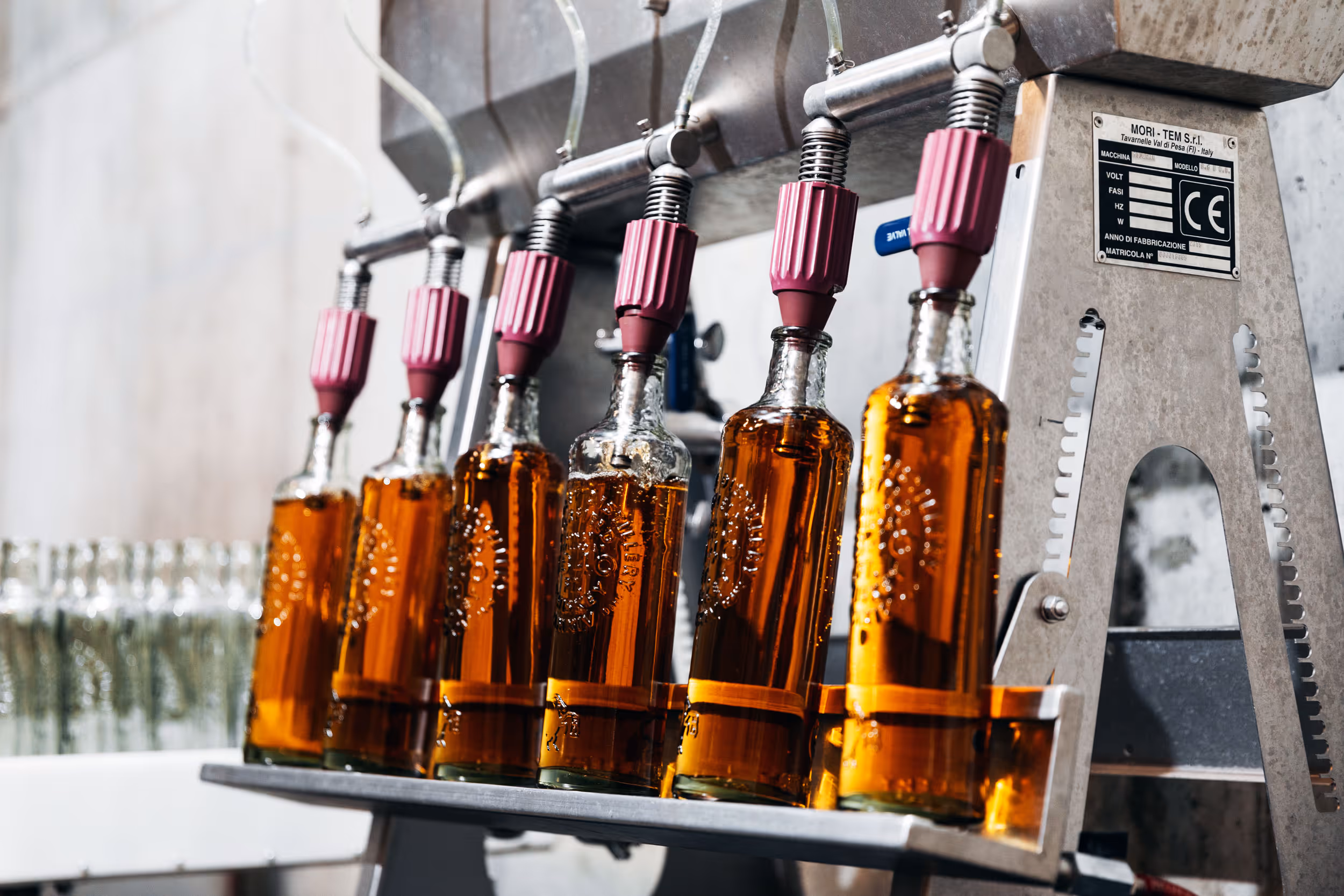 Glass bottles being filled with amber liquid by a bottling machine in a production line.