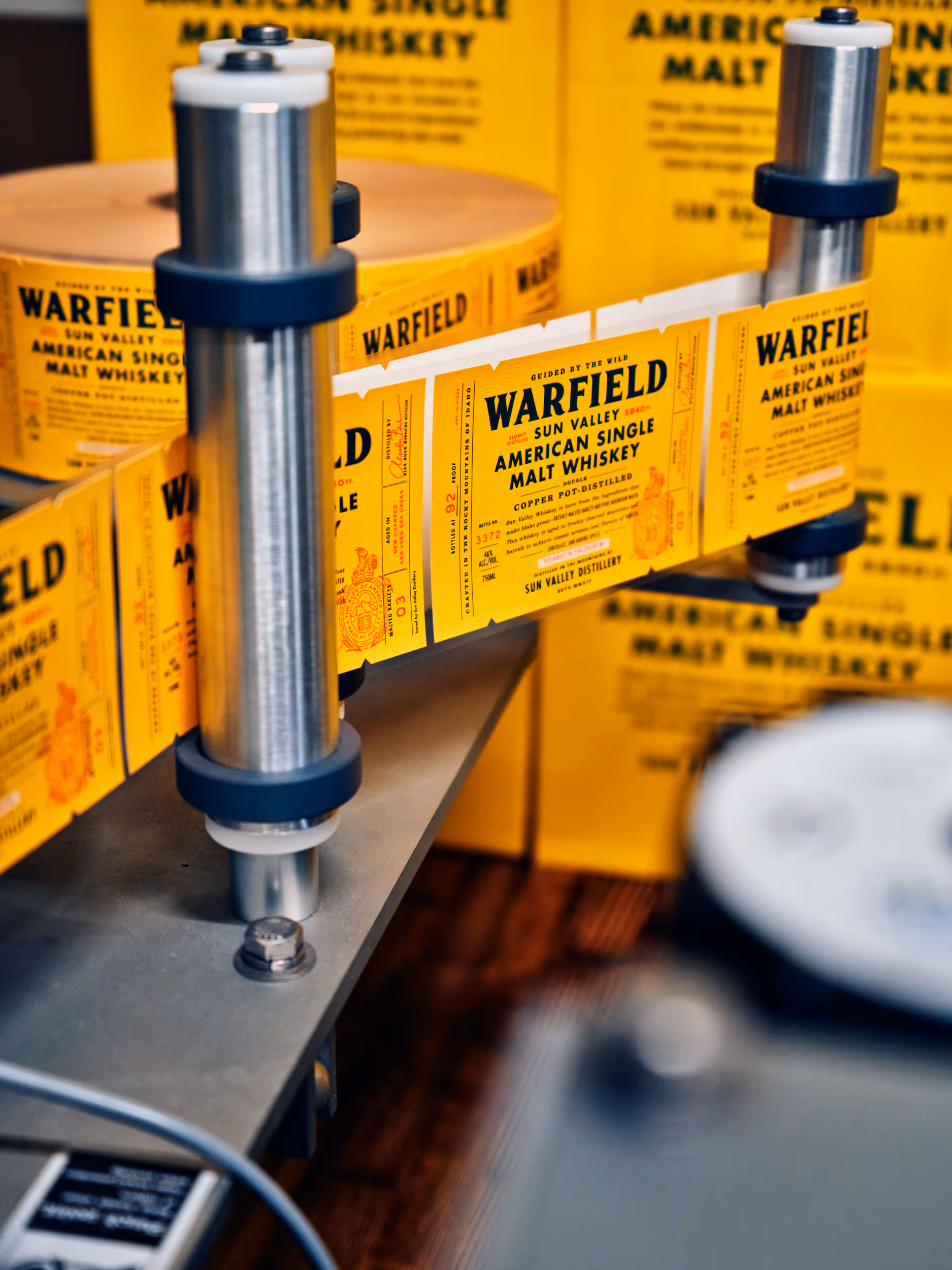 Close-up of a labeling machine applying yellow Warfield Sun Valley American Single Malt Whiskey labels.