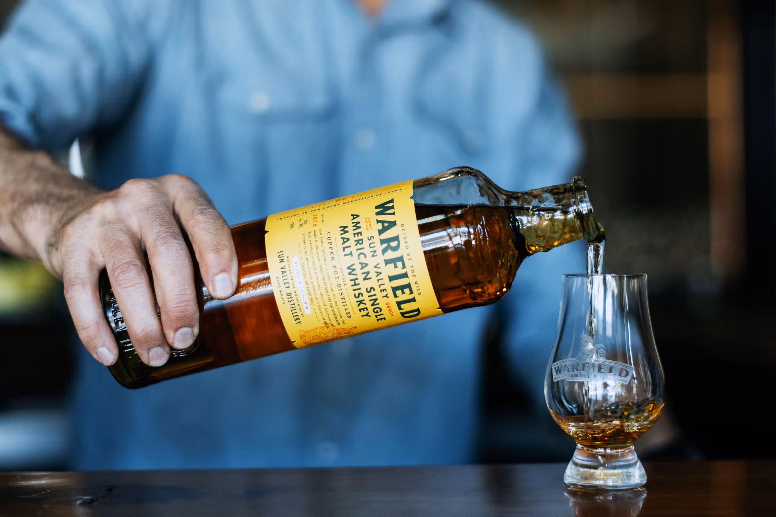 Person pouring Warfield American Single Malt Whiskey from a bottle into a branded whiskey glass.