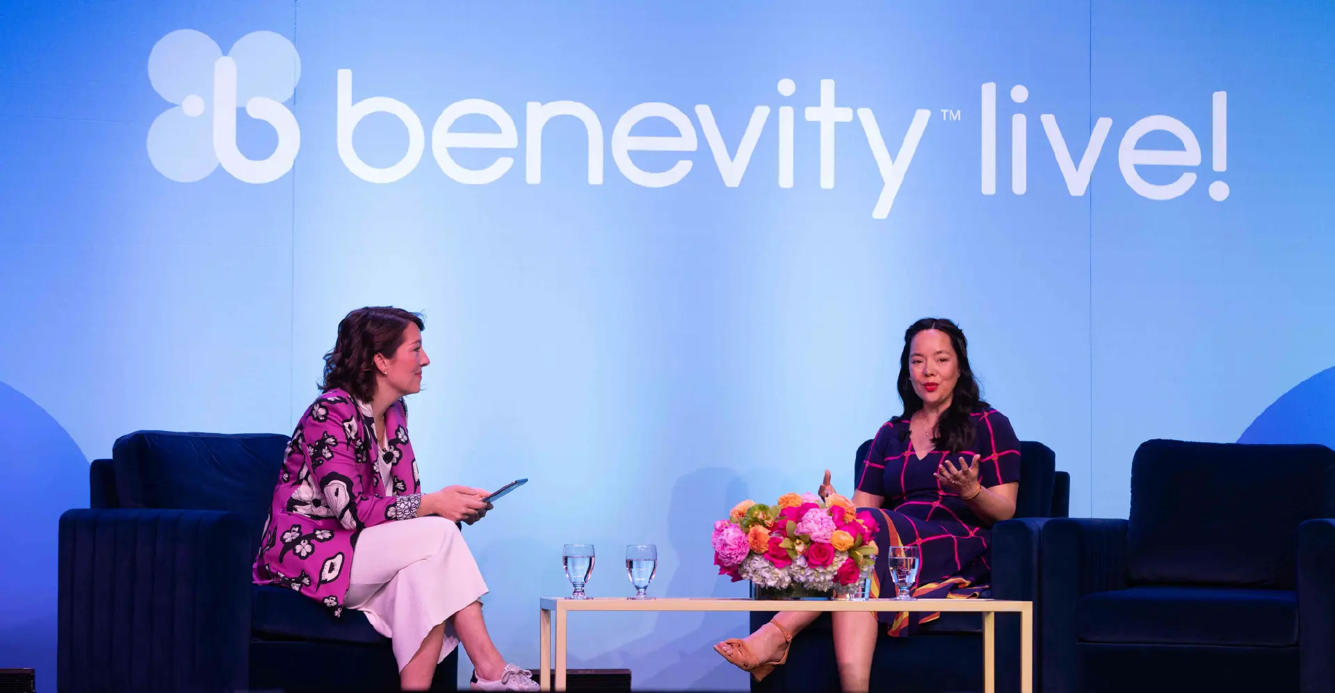 Two women seated on stage engaged in a conversation at a Benevity event.