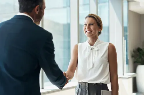 Smiling businesswoman shaking hands with a man in a bright office setting.