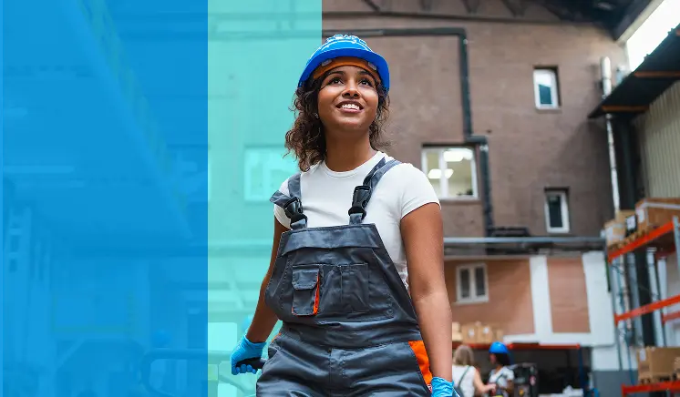 A woman wearing a blue hard hat, gloves, and overalls smiles while working in an industrial warehouse setting. Shelves and building materials are visible in the background. A blue transparent overlay is on the left side of the image.