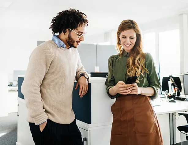 Man and woman smiling and looking at a phone in a bright modern office.