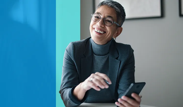 Smiling professional woman with short gray hair, glasses, and a dark blazer holding a smartphone.