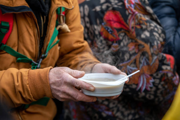 Person in a brown jacket holding a steaming bowl of hot soup with a spoon.