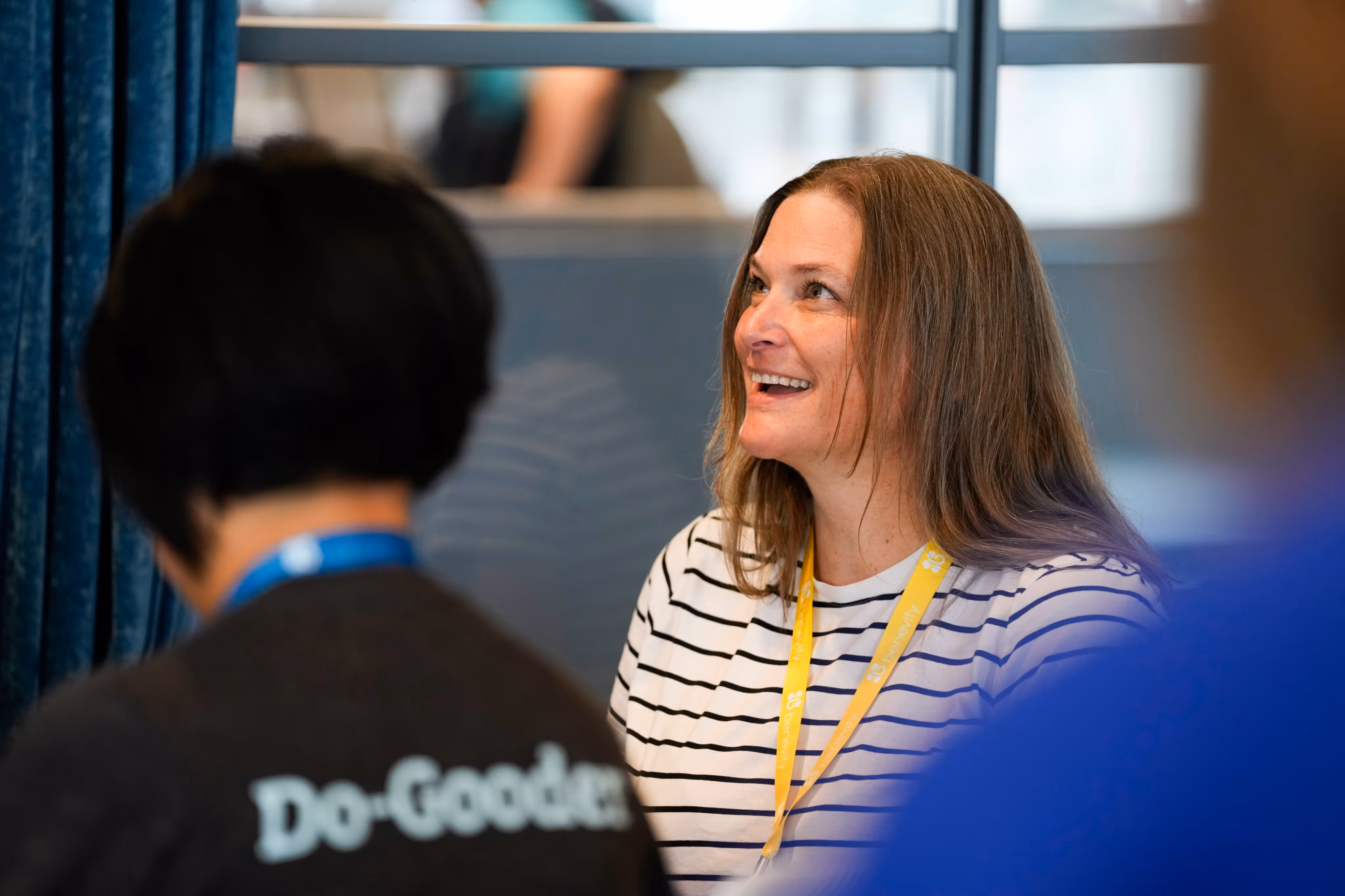 Smiling woman with shoulder-length brown hair wearing a striped shirt and yellow lanyard during a conversation.