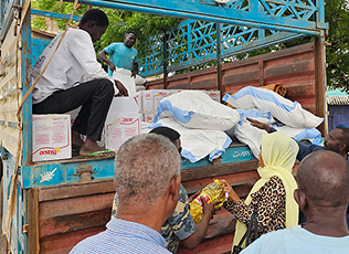 People around a truck distributing large white bags of supplies in an outdoor setting.