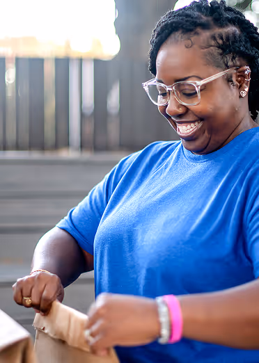 Smiling woman in a blue shirt packing items into a paper bag indoors.
