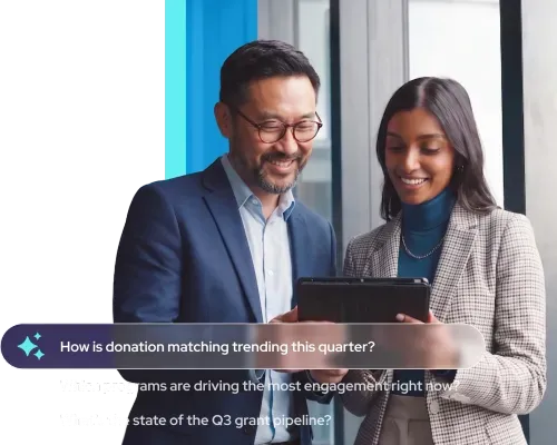 Smiling man and woman in business attire looking at a tablet in an office setting.