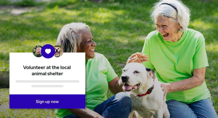 Two women in green shirts smiling and petting a white dog outdoors on grass.