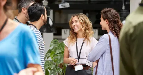 A group of people having a casual conversation indoors, with one woman in the center smiling.