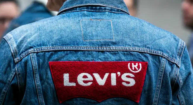 A person wearing a blue denim jacket with a large red and white Levi’s logo patch on the back. The image is focused on the upper back of the jacket.
