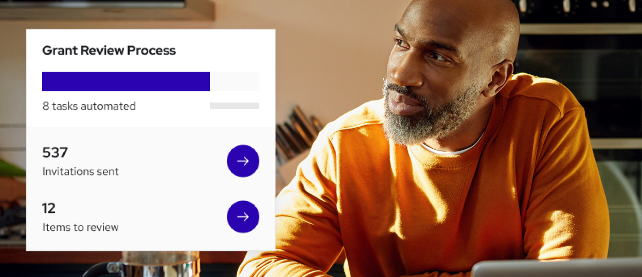 Man with a gray beard in an orange sweater looks right, to a stat of grant review process.