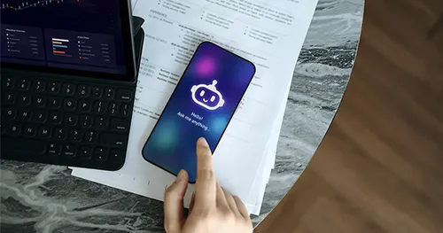 Person using AI chatbot next to laptop for work.