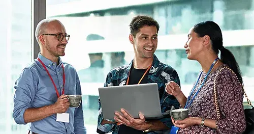 Three colleagues stand together by a window, smiling and talking.