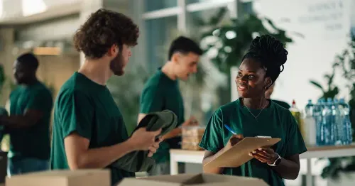 2 coworkers volunteering by organizing donations and talking to each other, the female is holding a clipboard.