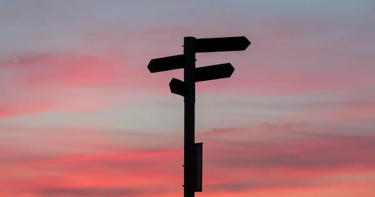 A silhouette of a signpost with multiple directional arrows stands against a pink and purple sunset sky, symbolizing getting started with CSR and choosing the right path forward.