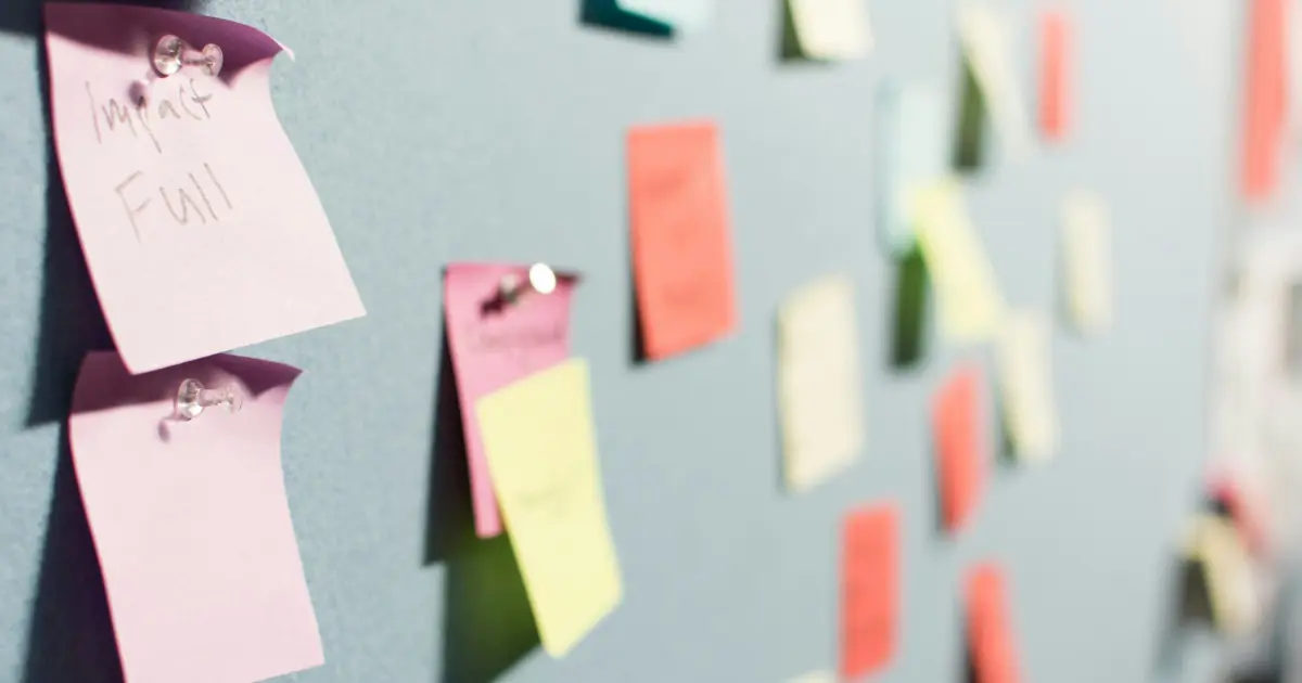 A close-up view of a bulletin board covered with colorful sticky notes and papers, some pinned and some overlapping, with handwritten notes visible on a few of them.