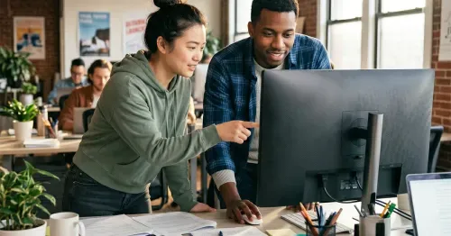 A man and woman looking at a computer screen in a bright office and having a discussion.
