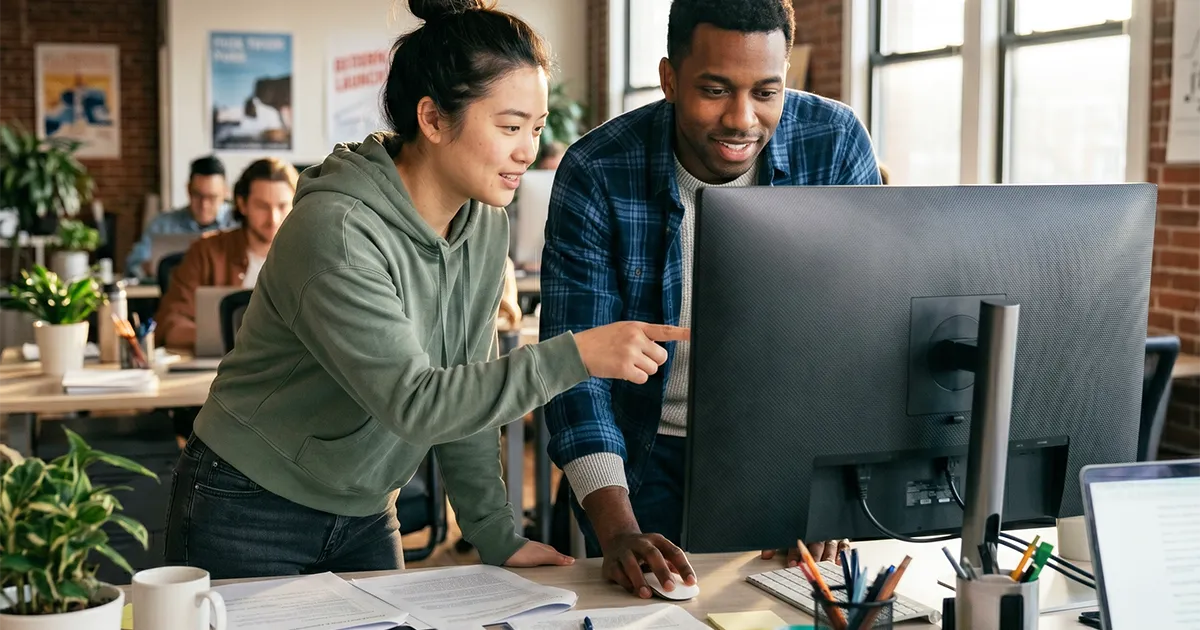 A man and woman looking at a computer screen in a bright office and having a discussion.