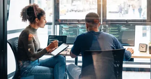 Two engineering employees working on coding in a bright office.