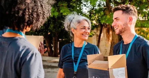 Smiling volunteers holding cardboard boxes during an outdoor community service event.