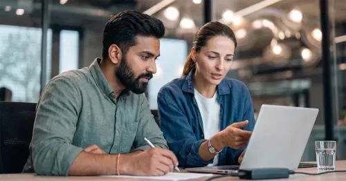 Male and female colleague in a modern office reviewing a computer screen, discussing the true costs of running purpose programs manually versus with a managed platform.