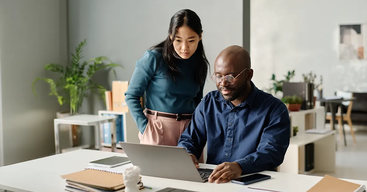 A male and female coworker reviewing a laptop in a bright modern office.