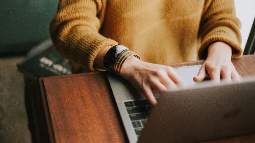 A person types on a laptop keyboard in a bright, modern workspace.