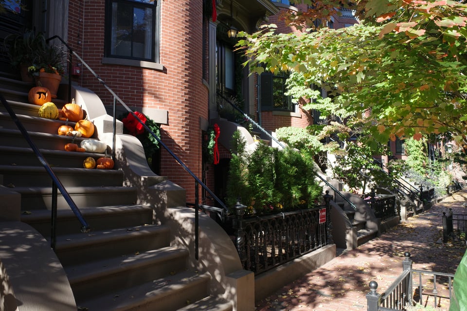 A row of brick townhouses, decorated with pumpkins on the steps and Christmas wreaths on the doors