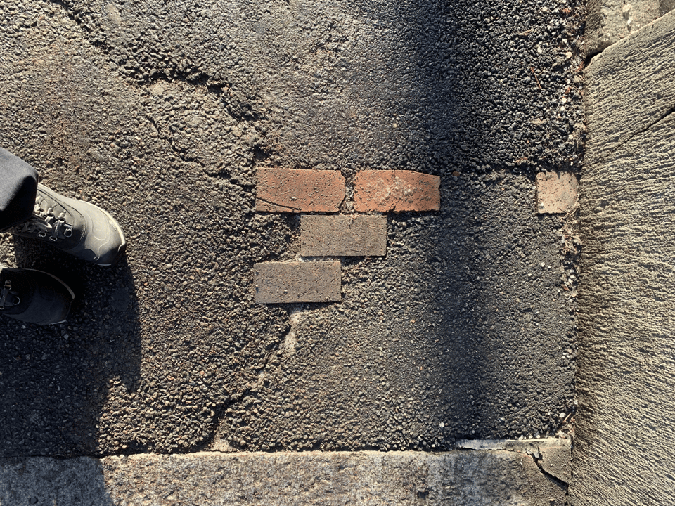 A close up of a sidewalk with a few stray bricks peeking through the surrounding asphalt