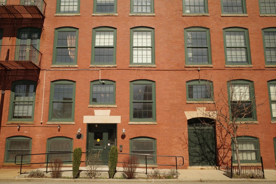 A brick building with green-trimmed windows and doorways, lit by soft afternoon sun.