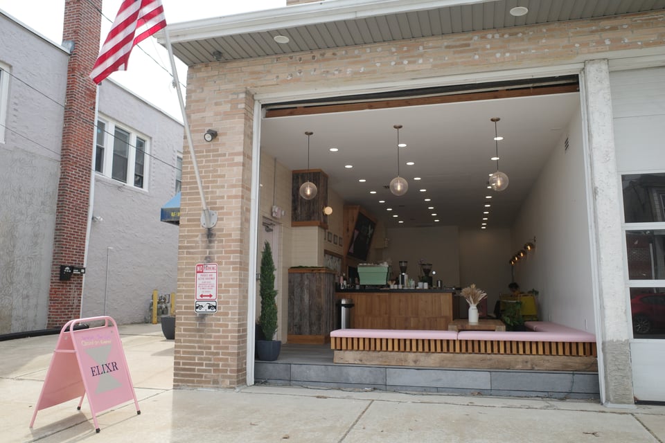 A former firehouse turned coffee shop now opens wide to the street, welcoming passersby with warm lighting and soft pink seating.