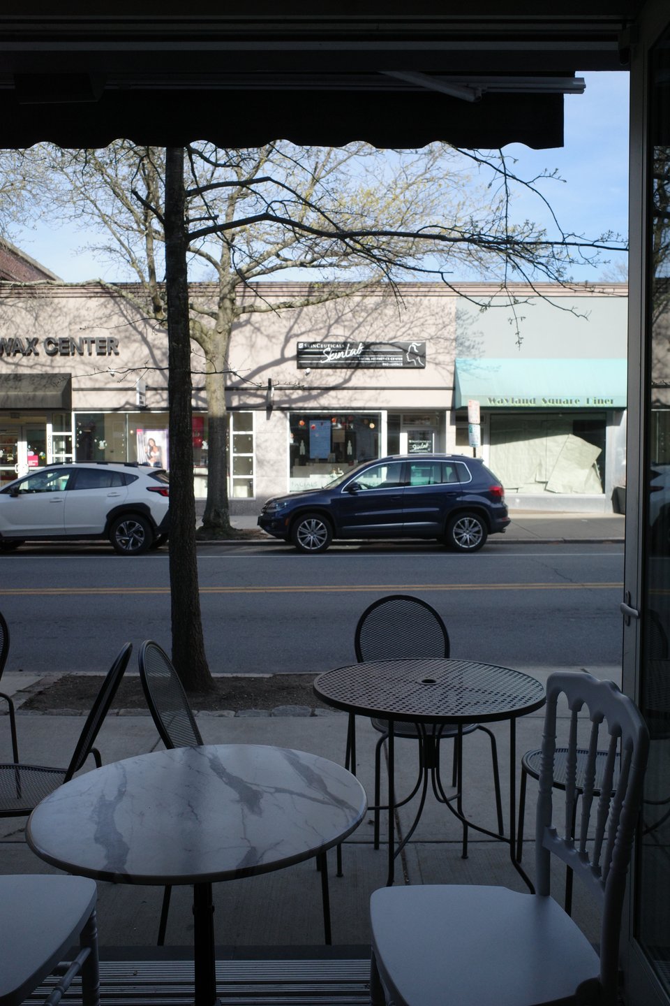 View from inside a café looking out at a quiet street with parked cars and shopfronts across the road.