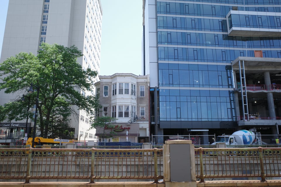 A small three-story brick storefront with bay windows wedged between two glass-and-concrete high-rises.