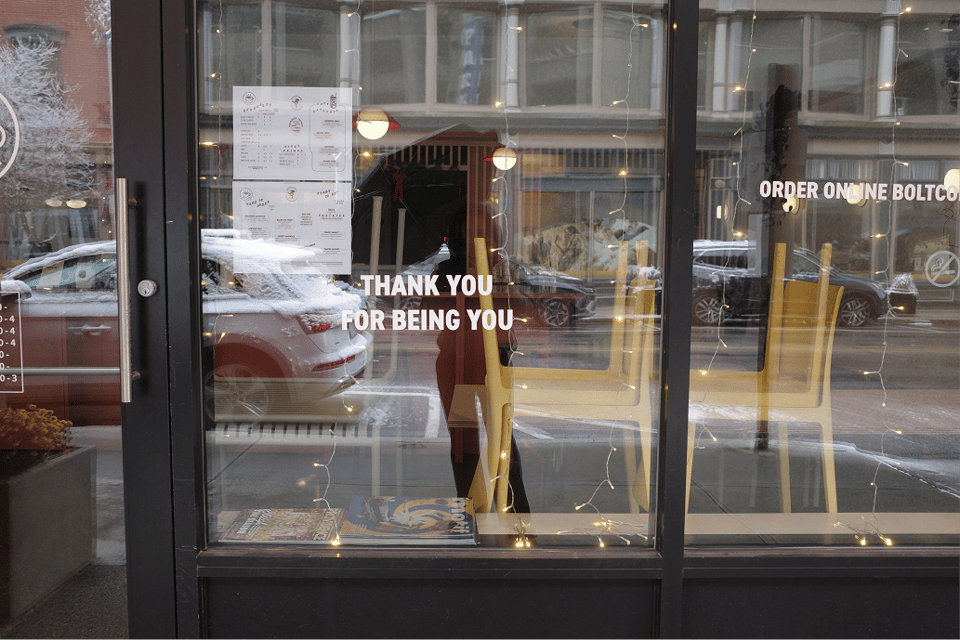 A café window with stacked chairs, string lights, and the message “thank you for being you”