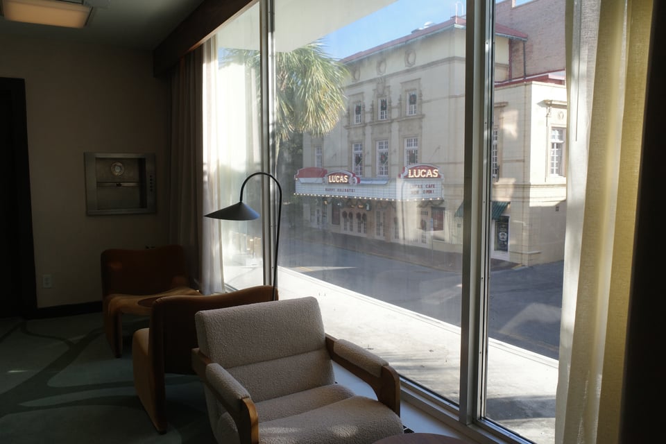 Mid-century armchairs by a large window overlooking a quiet street and theater marquee.