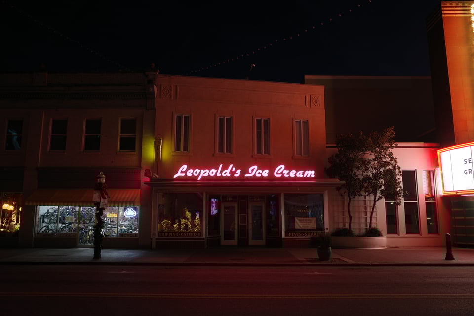 Neon “Leopold’s Ice Cream” sign glowing on a quiet street at dawn.