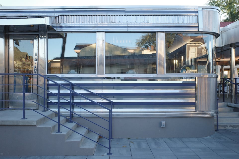 Exterior of a streamlined, metal-clad diner with curved corners and steps leading up.