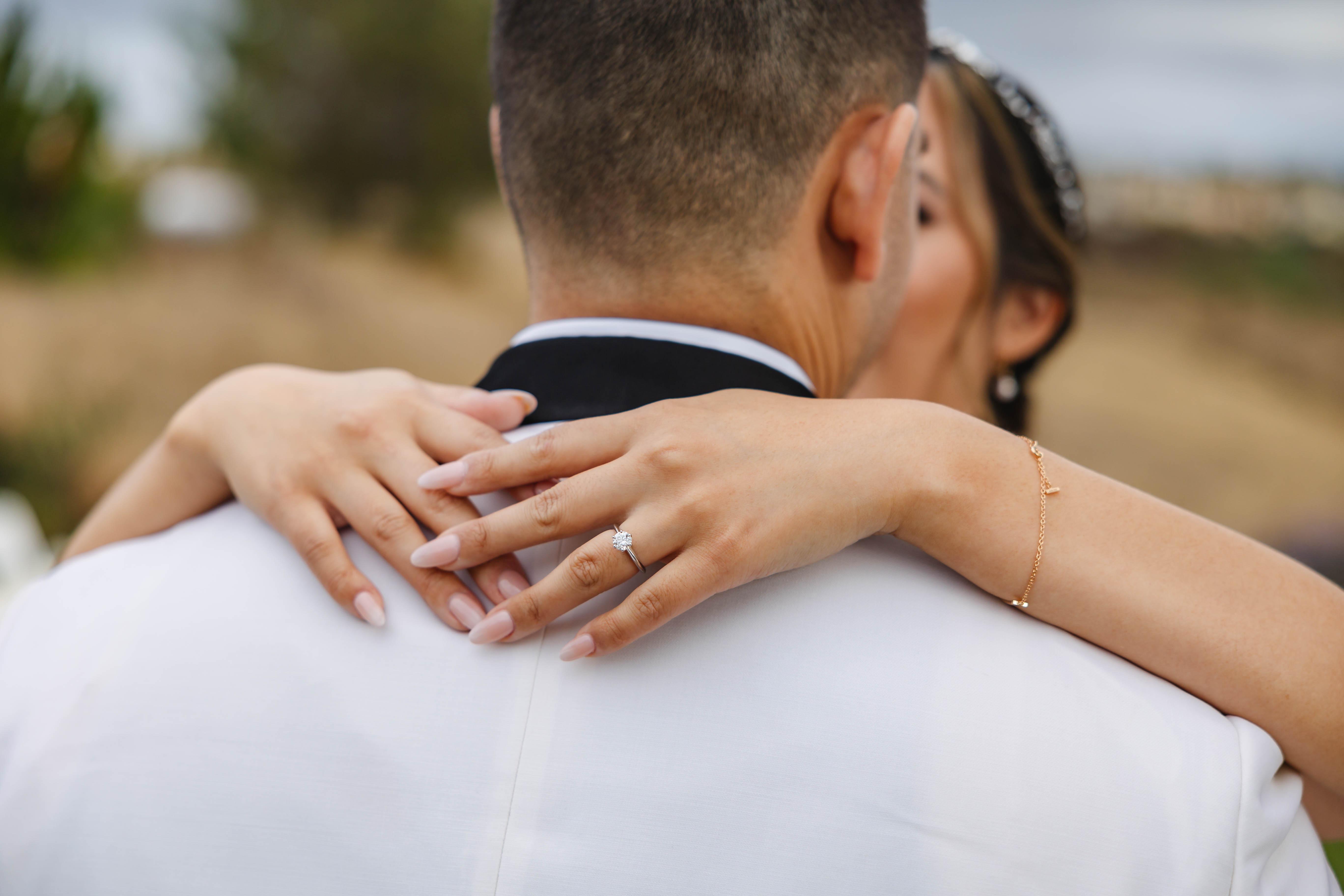 Bride embracing groom with engagement ring visible on her hand over his shoulder.