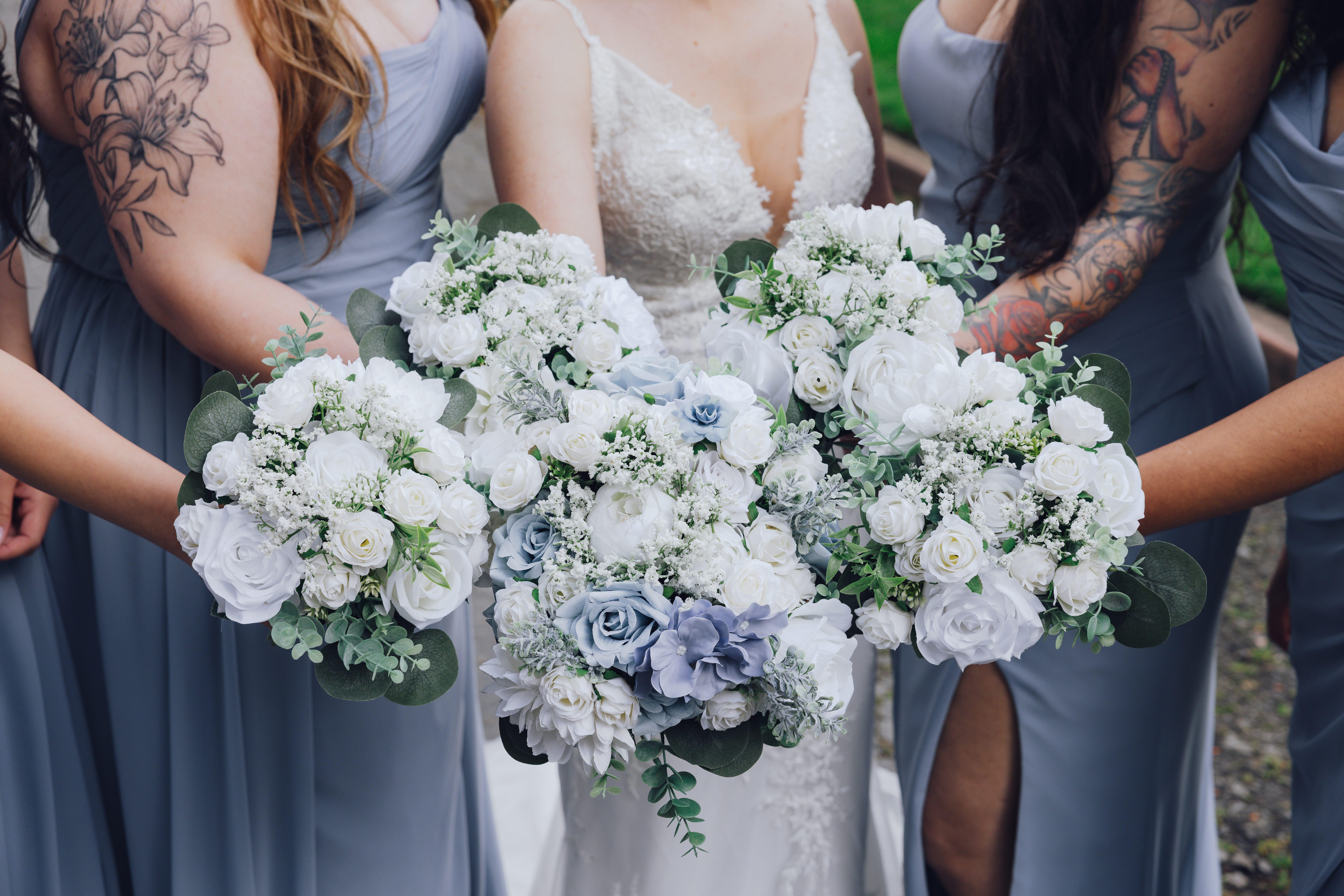 Bride and bridesmaids in blue dresses holding white and light blue floral bouquets.