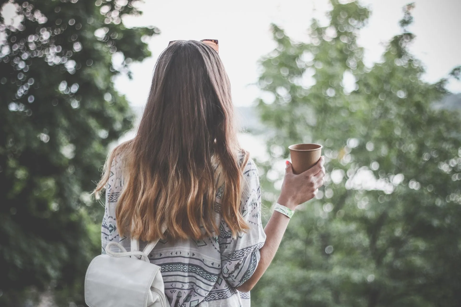 Picture of a person holding a coffee looking into the treeline