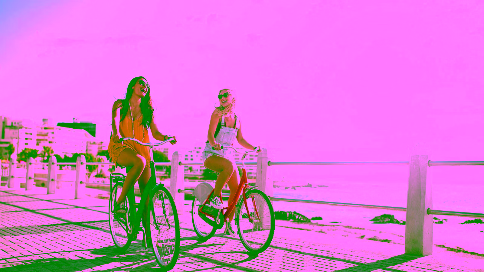 two girls smiling while riding bikes on a beach boardwalk